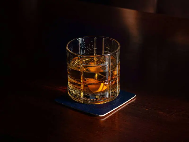 A glass of whiskey on top of a wooden table.