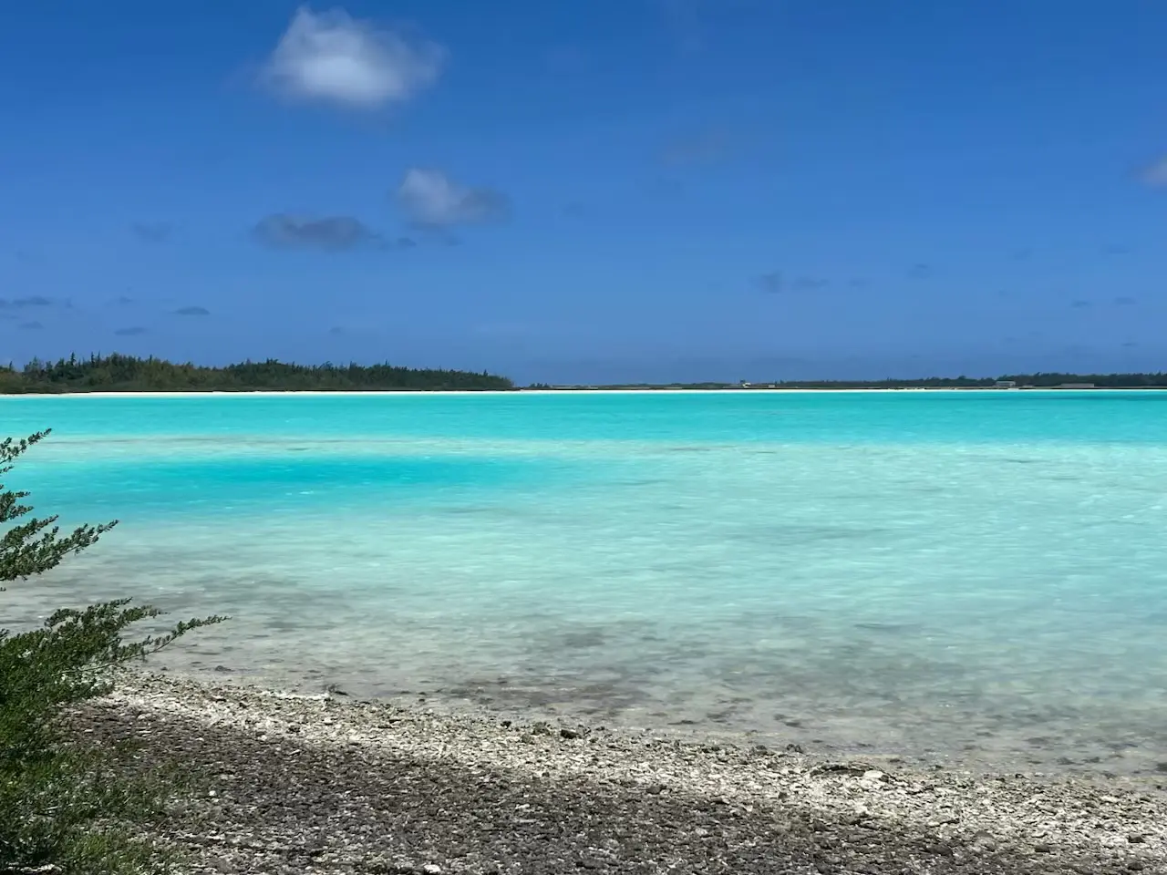 A serene turquoise lagoon with a rocky shore under a clear blue sky.